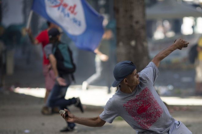 Протестующий против жесткой экономии бросает камень в полицию за пределами законодательного собрания штата, где законодатели обсуждают меры жесткой экономии в Рио-де-Жанейро, Бразилия, вторник, 6 декабря