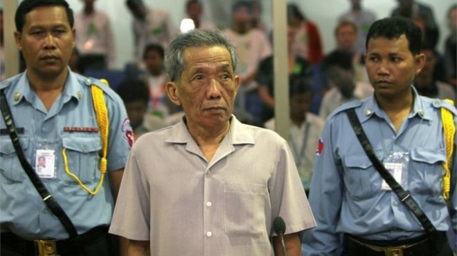 ФОТОГРАФИЯ: Бывший начальник тюрьмы S-21 красных кхмеров Кайнг Гек Ив, более известный как Дуч, стоит в зале суда во время предварительного следствия в Пномпене 5 декабря 2008 г.