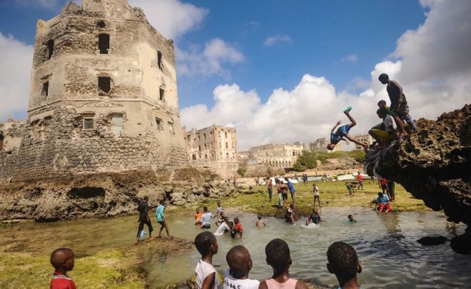 Сомалийские дети ныряют, играют и плавают перед руинами старого здания на берегу моря в Могадишо, Сомали - 2017