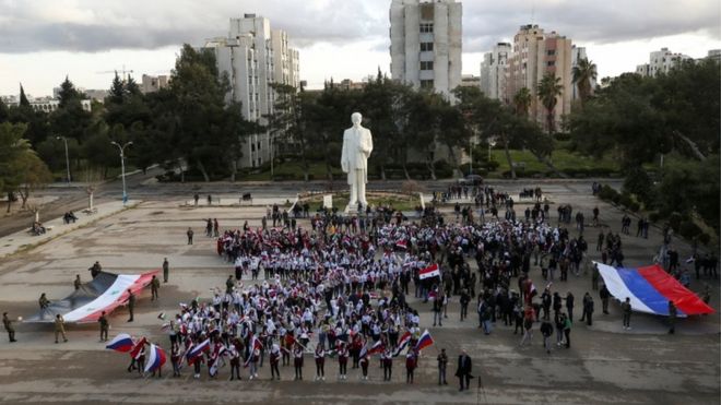 متطوعون سوريون أمام تمثال لحافظ الأسد في دمشق