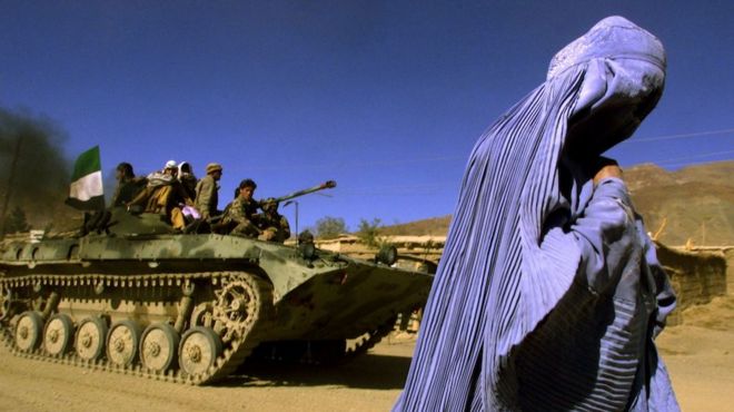 FILE PHOTO: An Afghan woman wearing a traditional burqa walks on the side of a road as a Northern Alliance APC, (Armoured Personnel Carrier) carrying fighters and the Afghan flag, drives to a new position in the outskirts of Jabal us Seraj, some 60kms north of the Afghan capital Kabul November 4, 2001. REUTERS/Yannis Behrakis/File Photo