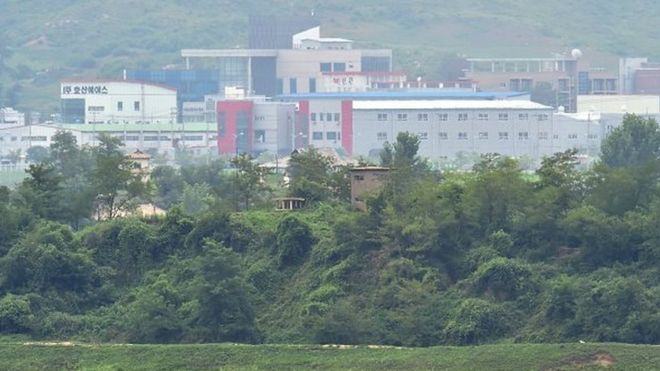 Северокорейский сторожевой пост (C) стоит перед межкорейским промышленным комплексом Кэсон (на заднем плане), как видно из перемирия в деревне Панмунжом в Демилитаризованной зоне, разделяющей две Кореи 22 июля 2015 года
