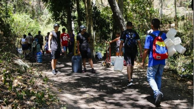 Люди ходят с цистернами и бутылками, чтобы наполнить их водой, которая поступает с горы во время отключений, что влияет на водяные насосы 12 марта 2019 года в Каракасе, Венесуэла.