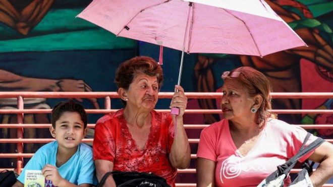 Un niño en una calle de Caracas sentado junto a dos mujeres mayores.