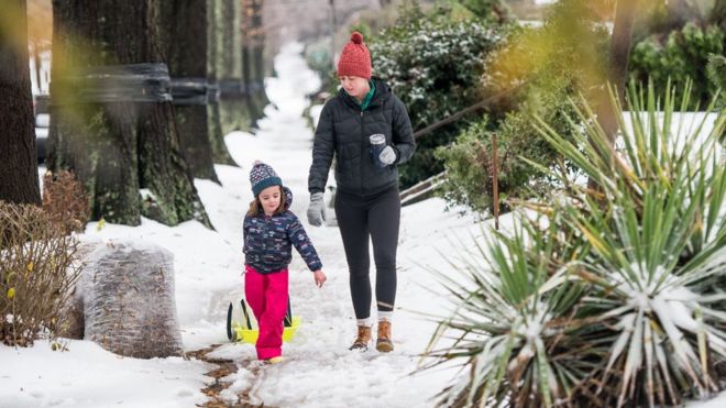Лорен (слева) и Анна Фарнхем прогуливаются по снегу по соседству 9 декабря 2018 года в Шарлотте, Северная Каролина