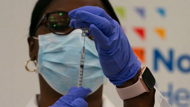 A healthcare worker fills a syringe from a phial