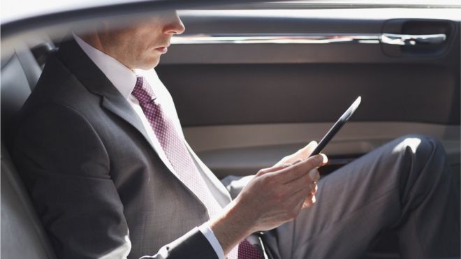 Hombre con traje leyendo en un dispositivo móvil y abordo de un auto de lujo