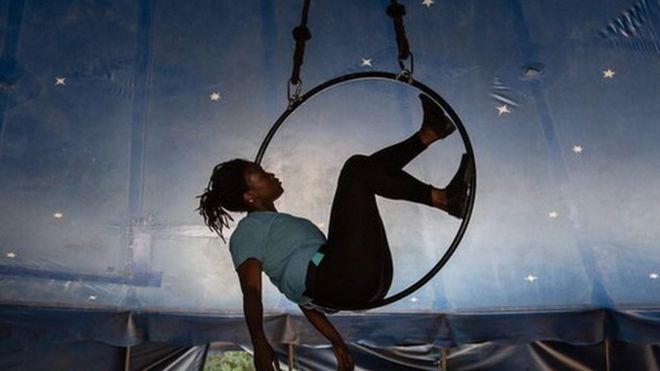 Femme acrobate en équilibre sur une roue suspendue. Elle se trouve dans un chapiteau de cirque.