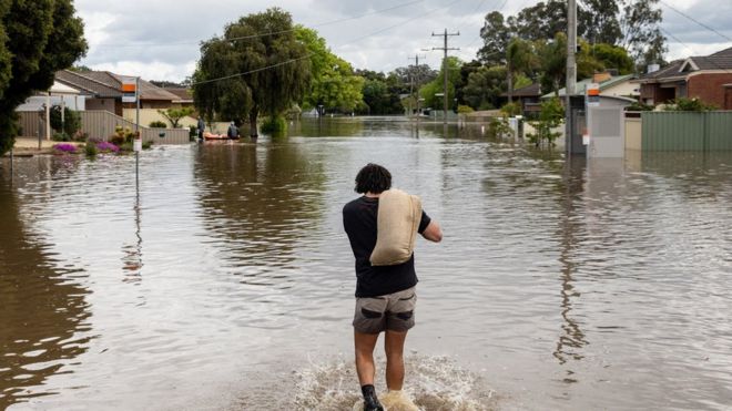 A local resident carries a sandbag through floodwaters as the state of Victoria faces an ongoing flood crisis, in Shepparton, Australia, October 16, 2022.