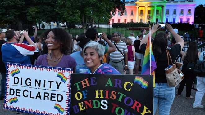 Активисты-геи держат вывески перед Белым домом, освещенным радужными цветами в Вашингтоне 26 июня. 2015