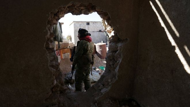 A rebel fighter stands near a hole in the wall as he carries his weapon on the outskirts of Al-Bab town in Syria