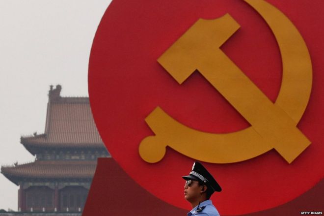 Полицейский патрулирует гигантскую коммунистическую эмблему на площади Тяньаньмэнь 28 июня 2011 года в Пекине, Китай