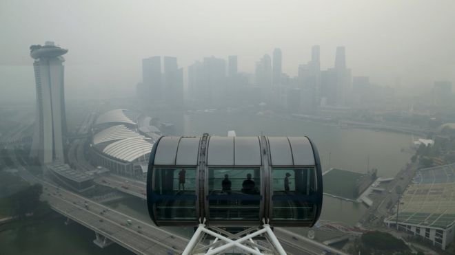 Туристы садятся в капсулу на колесо обозрения сингапурской летающей обсерватории с видом на горизонт центрального делового района, окутанного дымкой в ??Сингапуре 10 сентября 2015 г.