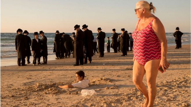Una mujer en bañador y un grupo de ultraortodoxos en una pleya cercana a Tel Aviv.