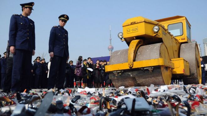 Местные полицейские и представители общественности наблюдают за тем, как дорожный каток раздавливает контрафактную продукцию 23 февраля 2011 года в Шанхае, Китай.
