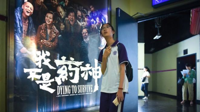 На этом снимке, сделанном 12 июля 2018 года, девушка проходит мимо плаката с фильмом «Умирающий, чтобы выжить» в кинотеатре в Пекине