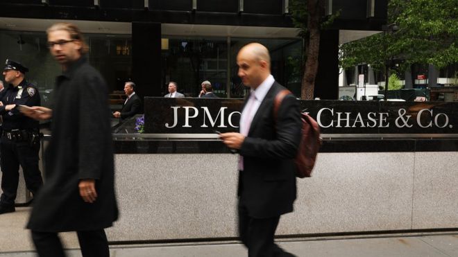Люди проходят мимо, в то время как другие протестуют перед штаб-квартирой JPMorgan Chase в Нью-Йорке 11 мая 2017 года в Нью-Йорке