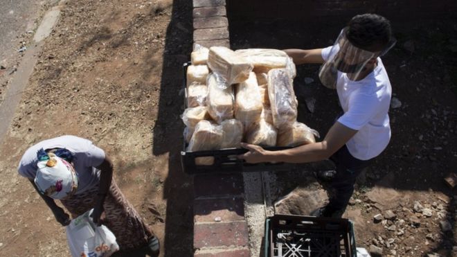 Homem com máscara e protetor visual distribui comida para população em situação de necessidade