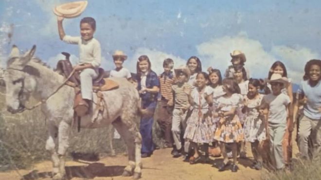Un grupo de niños sigue a un pequeño montado en un burro