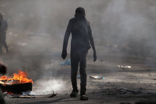 Ребенок закрывает лицо, проходя мимо горящей баррикады во время антиправительственных протестов в Порт-о-Пренсе