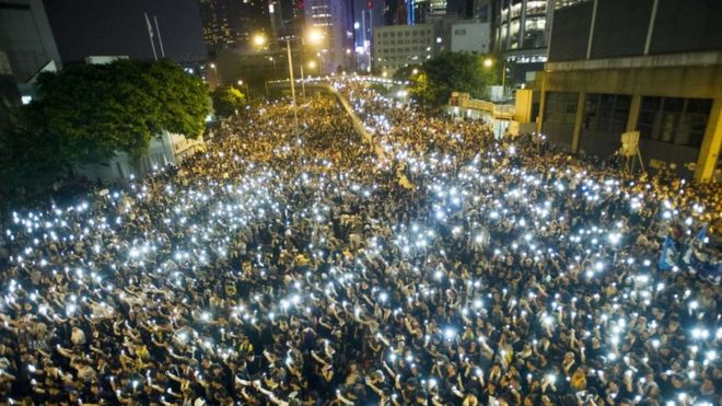 Протестующие и учащиеся-демонстранты держат свои мобильные телефоны в знак солидарности во время акции протеста перед штаб-квартирой Законодательного совета в Гонконге 29 сентября 2014 года.