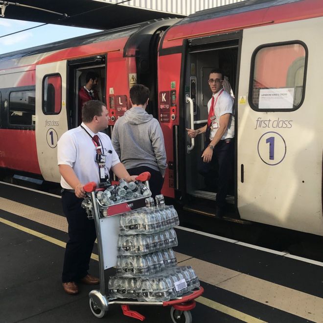 Сотрудник LNER толкает тележку с бутилированной водой на вокзале Питерборо, пока пассажиры ждут новостей во время перебоев на магистрали Восточного побережья после значительного отключения электроэнергии