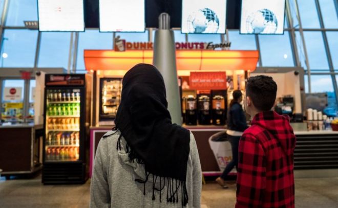 Молодая женщина в хиджабе смотрит на табло прибытия в нью-йоркском аэропорту имени Кеннеди