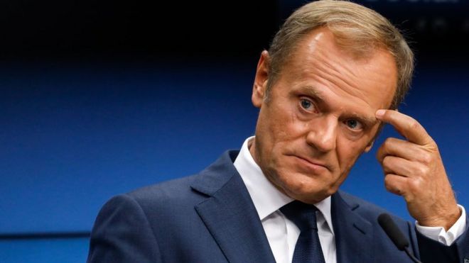 Donald Tusk gesturing with a finger to his forehead