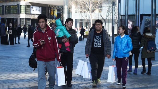 Люди, идущие мимо торгового центра с сумками в Пекине. Декабрь 2014