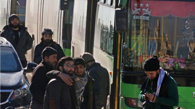Мужчины реагируют, когда они стоят возле автобусов, эвакуируя людей из удерживаемого повстанцами сектора восточного Алеппо