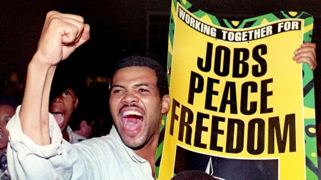 Сторонник цветной (смешанной расы) выкрикивает лозунги про Нельсона Манделы, держа здесь плакат с манифестом предвыборного штаба АНК на митинге избирательной кампании в Промозе, цветном городке возле Потчефструма в западном Трансваале, Южная Африка, 30 января 1994 года.