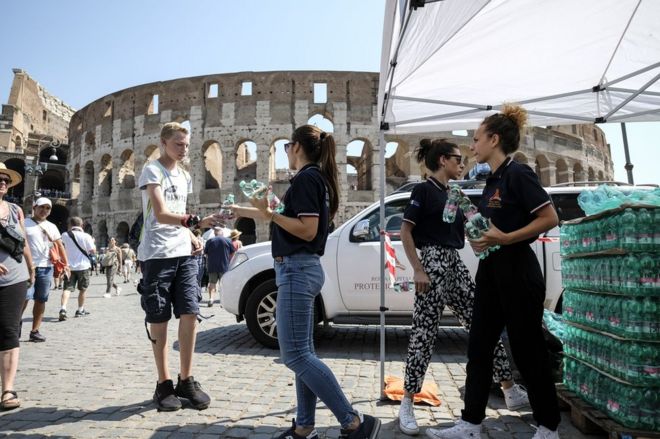 Члены Итальянской гражданской защиты (Protezione Civile) раздают бутылки с водой людям перед Древним Колизеем в центре Рима