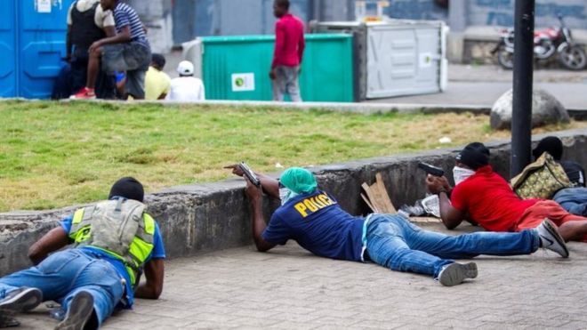 Вооруженные люди укрываются во время столкновений в Порт-о-Пренсе, Гаити, 23 февраля 2020 года.