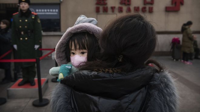 Child in Beijing wearing a protective mask, being carried by a relative