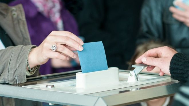 Женская рука укладывает бюллетень в урну для голосования