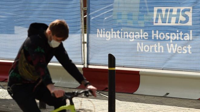 Мужчина в маске проезжает мимо Северо-западной больницы NHS Nightingale в центре Манчестера