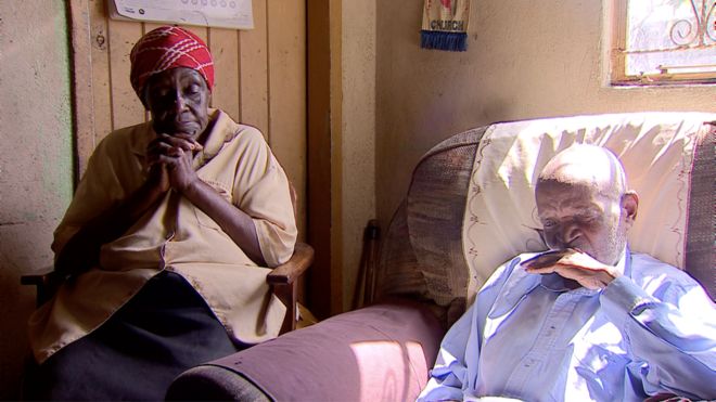 Vesta (L) and Teddy are a married couple. They sit on chairs in their home in Zimbabwe.