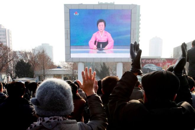 Северокорейцы смотрят новости о тестировании на видеоэкране возле железнодорожного вокзала Пхеньяна