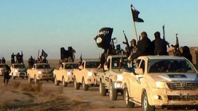 Undated photo shows militants of the Islamic State group hold up their weapons and wave its flags on their vehicles in a convoy on a road leading to Iraq, while riding in Raqqa city in Syria