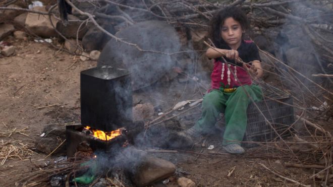 Syrian refugee Aysha Elwan, 5, helps her mother to break wood for a fire outside her family's tent at an informal settlement on the Syria-Jordan border at Mafraq