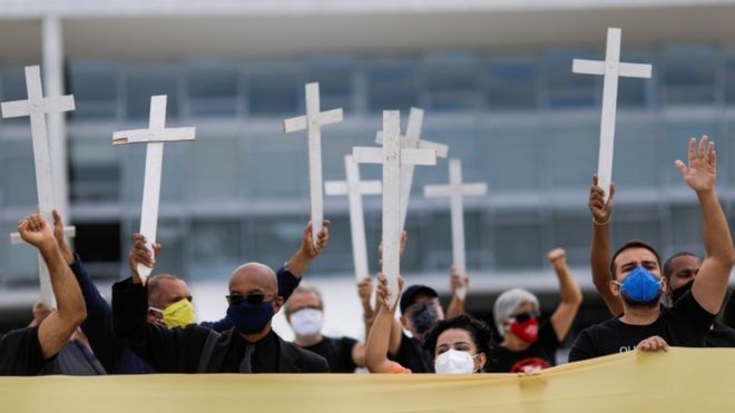 Pessoas com mscara levantando cruzes em protesto