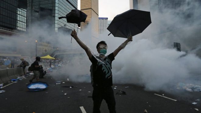 Протестующий держит зонт среди слезоточивого газа