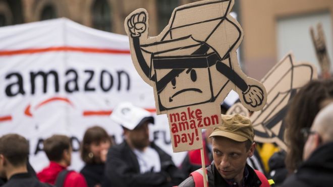Люди держат плакаты во время демонстрации, на которой присутствуют представители Amazon-Workers, профсоюзы и участники акции под девизом «Сделай Amazon Pay Pay» в Берлине, Германия, 24 апреля 2018 года.