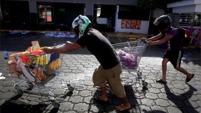 Торговцы позируют для фотографии перед входом в свой бизнес, поскольку они держат оружие, чтобы предотвратить мародерство протестующими в Манагуа, Никарагуа, 22 апреля 2018 года