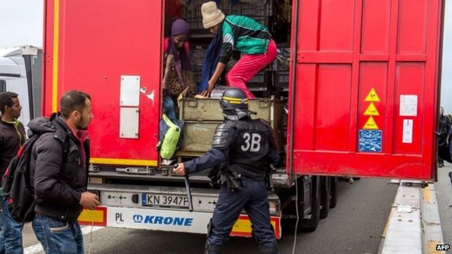 Французский полицейский стоит за грузовиком, когда мигранты поднимаются со спины