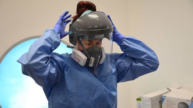 Член клинического персонала надевает средства индивидуальной защиты (СИЗ), включая козырек, маску, халат и перчатки в отделении интенсивной терапии больницы Royal Papworth в Кембридже, 5 мая 2020 г.