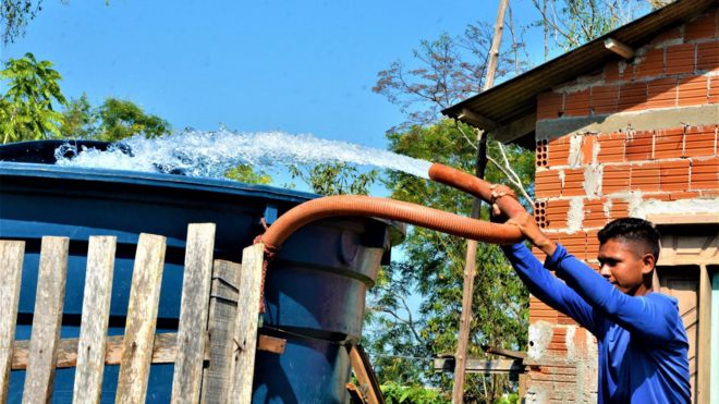 Trabalhador enchendo caixa d'água a partir de caminhão-pipa em Rio Branco, no Acre