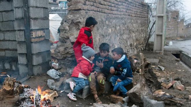 چهار کودک بیرون از آوار نزدیک آتش نشسته‌اند
