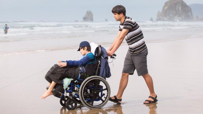 Persona mueve a un niño en silla de ruedas por la playa