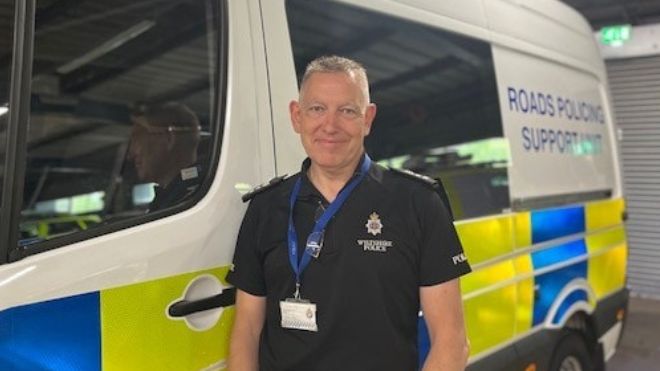 Sgt Rich Hatch in uniform standing beside a police van that says 'Roads Policing Support Unit' on it.